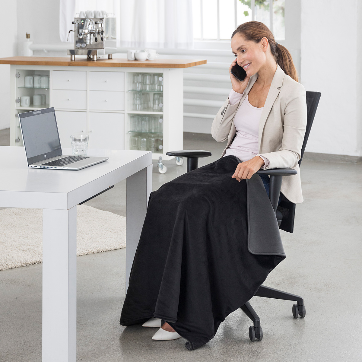 Businesswoman using an electric heated lap blanket in the office to stay warm and comfortable while working